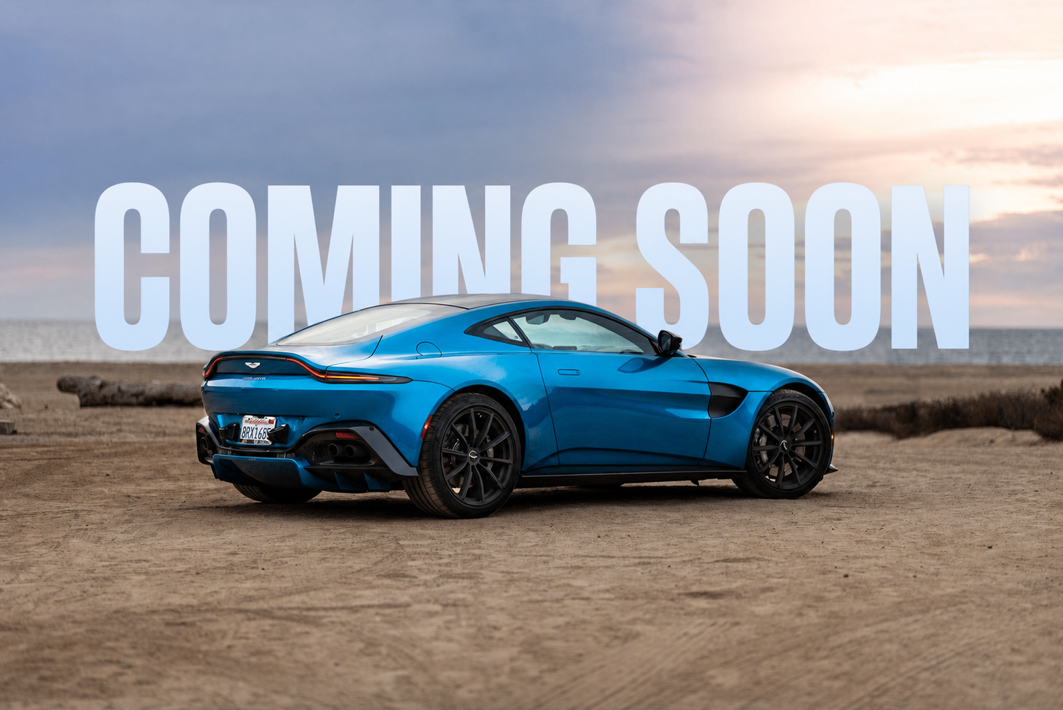 Coming Soon behind a blue performance coupe parked beside the ocean